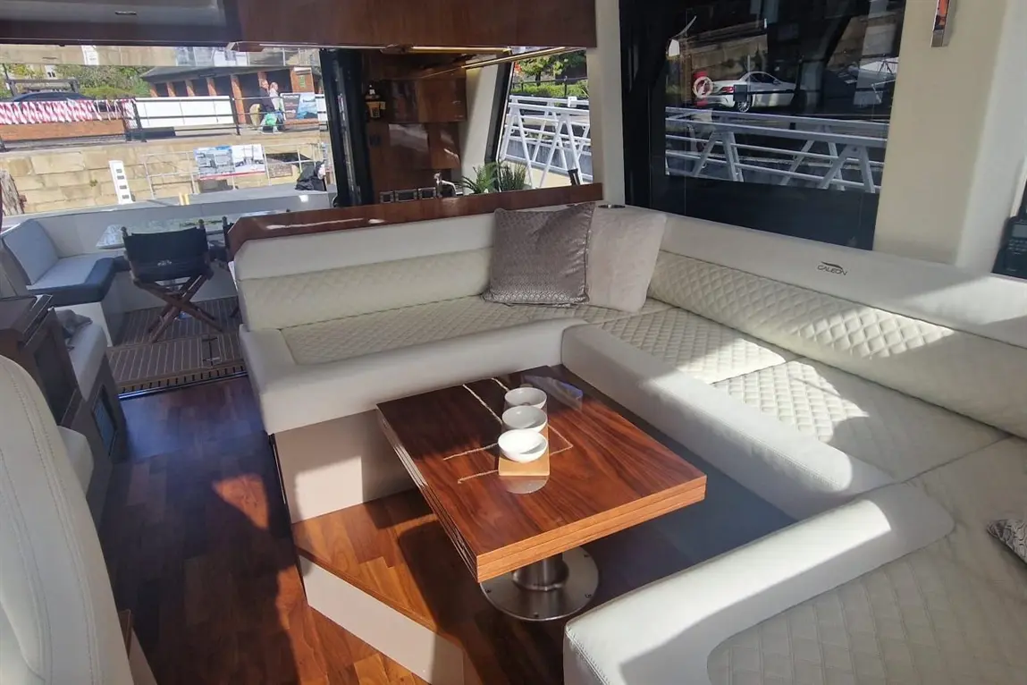 Luxurious interior of a yacht featuring white leather seating, a wooden table with cups, and large windows overlooking the dock.
